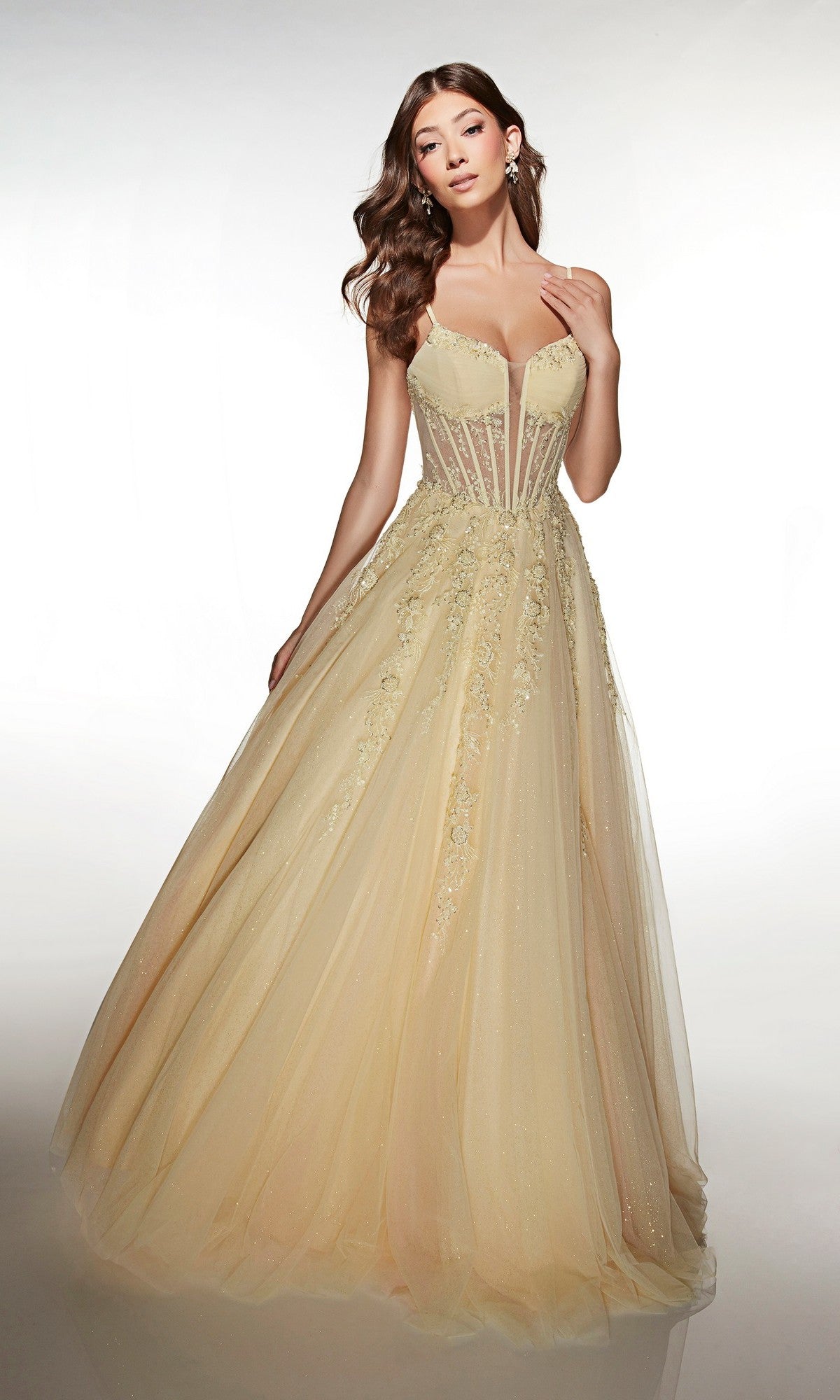 A woman stands against a plain background wearing the Alyce 62061 long prom dress in light yellow/pink, featuring a sleeveless fitted lace corset bodice with floral embellishments and a tulle ballgown skirt for an elegant look.